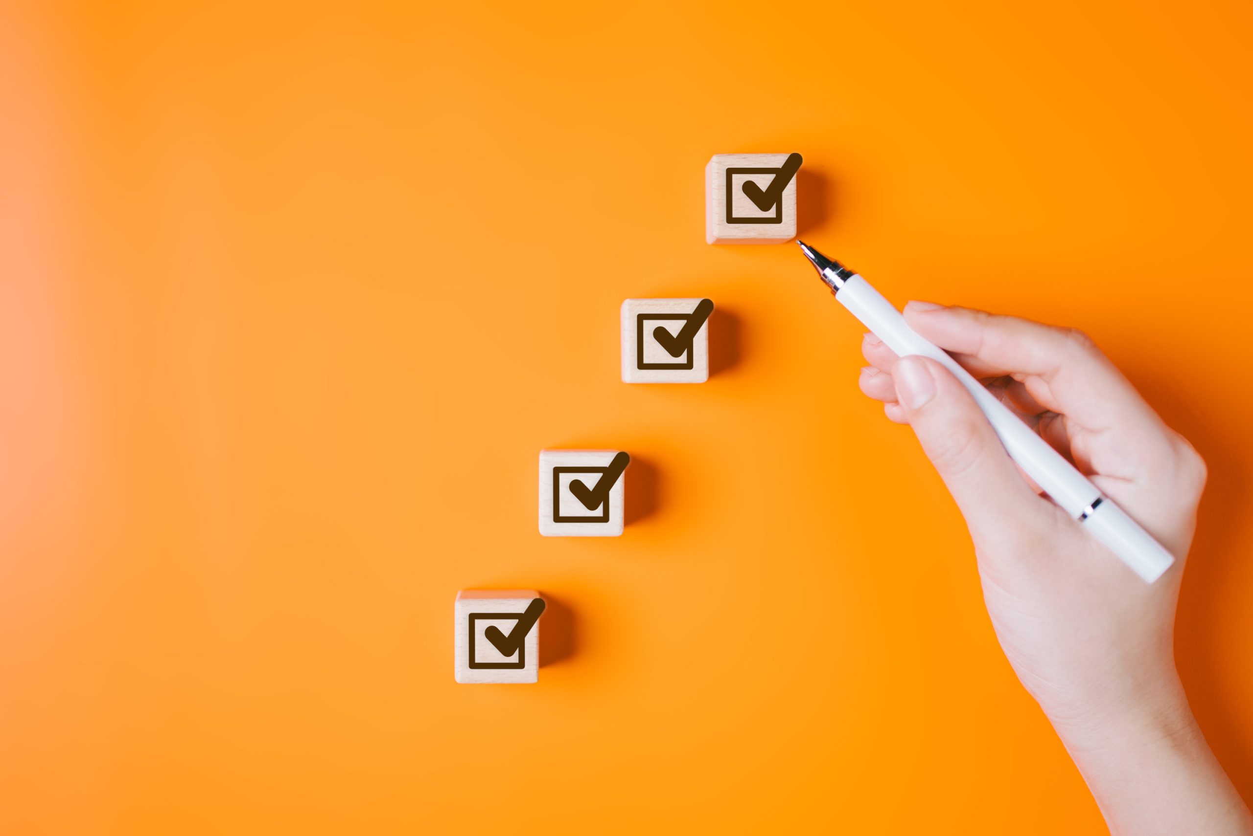 Hand placing a checkmark block on an orange background, representing a strategic tax preparation checklist