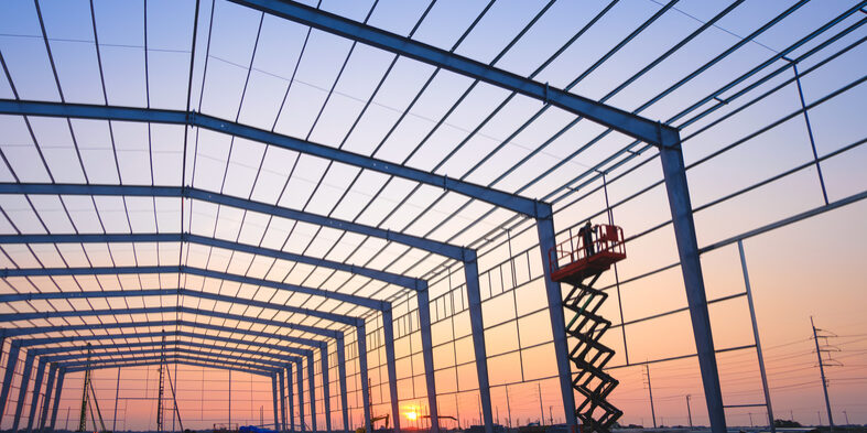 Silhouette factory building framework with welder worker on electric scaffolding working overtime to welding aluminium pipe on wall structure in construction site against sunset sky background