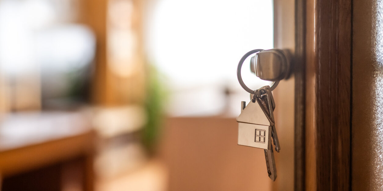 House-shaped keys are hanging from the door knob of a new home, representing the exciting moment of acquiring property and starting a fresh chapter