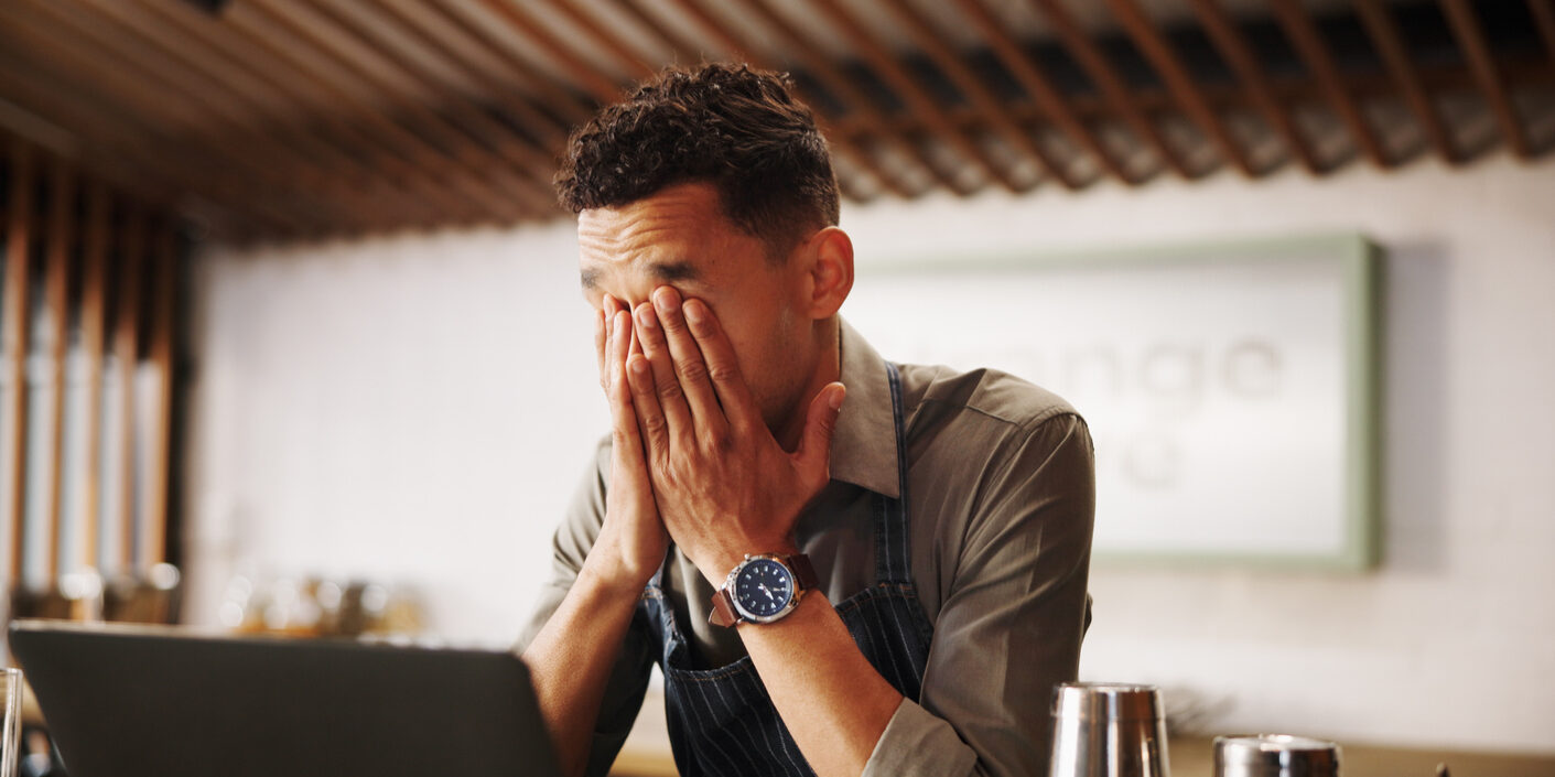 Frustrated man, barista and laptop with mistake for fatigue, eye strain or company bankruptcy at restaurant. Male person, bartender or overworked on computer for fail, loss or debt at indoor bar