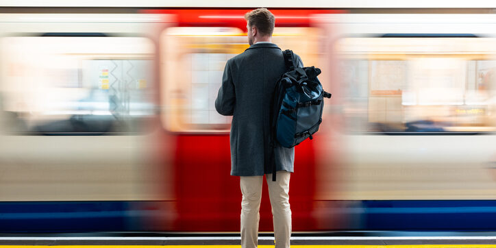 Man with backpack standing on a platform, watching a speeding subway train with motion blur in London. Mind the gap text visible