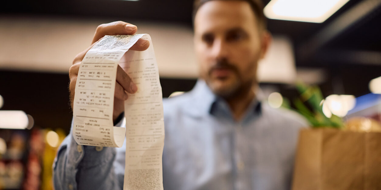 Close up of man going through grocery prices on a bill at the store.